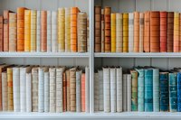 Collection of vintage and antique books arranged on white wooden shelves, featuring warm orange, yellow, white and turquoise spines creating aesthetic library display.