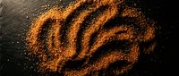 Golden turmeric powder arranged in decorative swirl pattern on dark slate surface creating artistic spice design for culinary and wellness applications.