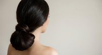 Elegant woman with dark hair styled in low chignon bun showing bare shoulders and neck from behind against neutral background for beauty and fashion concepts.