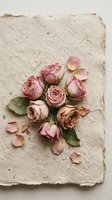 Dried pink roses arranged on handmade paper with scattered petals creating romantic vintage composition for wedding invitations and craft projects.
