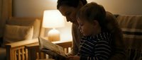 Father and young son reading book together on couch in warm evening light, family bonding time at home creating precious memories and learning moments.