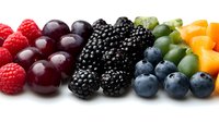 Fresh colorful berries arranged in rainbow pattern on white background - raspberries, cherries, blackberries, blueberries and citrus fruits. Clean isolated food photography.