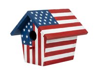 Wooden birdhouse painted with patriotic flag stripes and stars, isolated on white background, ready for home decor and garden design projects.
