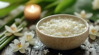Aromatic bath salt in ceramic bowl with jasmine flowers and glowing candle on dark wooden surface creates relaxing spa atmosphere for wellness and beauty.