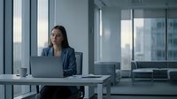 Professional businesswoman working on laptop in modern office with city view through large windows during daytime for corporate presentations.