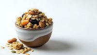 Homemade granola with nuts, dried fruits and oats in ceramic bowl on white background. Healthy breakfast cereal mix for morning meal preparation.
