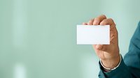 Man in business attire holding blank white card against mint green background, suitable for corporate branding, business card mockups, and professional presentations.