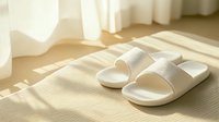 White comfortable home slippers on beige carpet with morning sunlight and shadow patterns from window, creating cozy minimalist atmosphere for lifestyle design.
