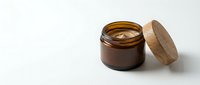 Amber glass jar with wooden lid containing golden cosmetic cream or balm, isolated on white background for skincare product packaging and beauty design use.