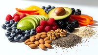 Colorful assortment of fresh fruits, nuts and seeds including avocado, berries, citrus and almonds arranged on white background for healthy eating concepts.