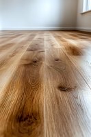 Natural oak hardwood flooring with distinctive grain patterns and knots viewed from ground level perspective against white walls, showcasing warm wood tones.