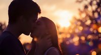 Romantic couple sharing intimate moment at golden hour sunset with warm bokeh lights creating dreamy atmosphere for love and relationship concepts.