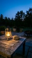 Glowing vintage kerosene lantern on rustic wooden table beside a love stone at dusk, cozy outdoor patio with fire pit and trees.