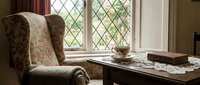 Cozy vintage reading nook with floral wingback chair beside wooden desk near diamond-paned window for home decor and interior design concepts.