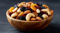 Wooden bowl filled with mixed nuts and dried fruits including cashews, almonds, raisins and apricots on dark background for healthy snacking concepts.