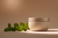 Natural skincare cream jar with fresh mint leaves on warm beige background for organic beauty and wellness products.