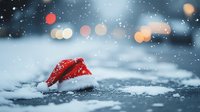 Red and white Santa hat lying in snow during snowfall with blurred bokeh lights creating magical winter holiday atmosphere. Festive Christmas background.