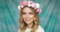 Young blonde woman wearing pink and white pom pom headband smiling at camera against turquoise backdrop for fashion and lifestyle photography.