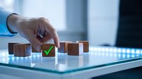 Hand selecting wooden cube with green checkmark from row of blocks on modern glass surface representing business decision making and quality control processes.