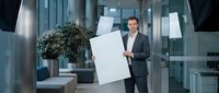 Professional businessman in dark suit presenting blank white boards in modern glass office lobby for corporate training and business presentations.
