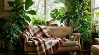 Cozy leather sofa with plaid throw blanket surrounded by lush green houseplants near bright window, creating warm, inviting interior design for home decor and lifestyle content.