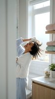 Young African American woman in bathrobe stretching arms up in bright modern bathroom with white subway tiles and natural light for morning wellness routine.