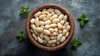 White butter beans in wooden bowl garnished with fresh mint leaves on dark stone background, overhead view of healthy legumes for cooking and nutrition.