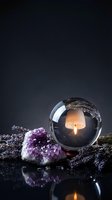 Crystal ball with burning candle flame inside surrounded by purple amethyst geode and dried lavender herbs on reflective surface for mystical divination.