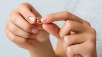 Female hands holding gold wedding ring against neutral background, symbolizing marriage proposal, commitment, and relationship milestone.