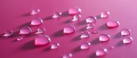 Water droplets in various sizes scattered across a vibrant pink surface, creating reflective spheres with soft shadows for cosmetic and skincare product backgrounds.