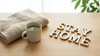Stay home wooden letters on a table with a cup of green tea and cozy knit blanket, promoting comfort and relaxation at home.
