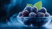 Fresh ripe blackberries and raspberries in glass bowl on dark blue background with dramatic lighting and fog effect, macro food photography.