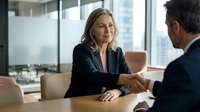 Professional businesswoman shaking hands with male colleague in modern office meeting room during successful negotiation or partnership agreement.