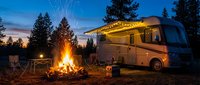 Modern RV motorhome parked at scenic campsite with crackling campfire under starry twilight sky surrounded by pine trees for outdoor adventure vacation.
