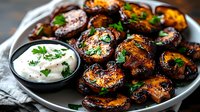 Grilled eggplant slices with charred edges, garnished with fresh herbs and served alongside creamy yogurt dip on gray plate. Mediterranean appetizer with smoky flavors.