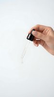 Hand holding glass dropper with liquid drop isolated on white background for skincare cosmetic and laboratory use.