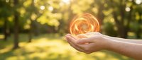 Hands holding glowing energy orb with warm light in natural outdoor setting with bokeh background for wellness and spiritual concepts.