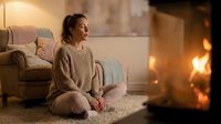 Young woman in cozy sweater sitting peacefully by warm fireplace in comfortable living room during evening relaxation time at home.