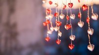 Romantic heart-shaped decorations hanging on strings with warm bokeh lights creating cozy Valentine's Day atmosphere for love celebration backgrounds.