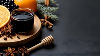 Aromatic mulled wine with orange slices, star anise, honey dipper and winter spices on rustic wooden board against dark background. Perfect for seasonal menu.