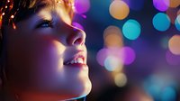 Young woman's face illuminated by colorful bokeh lights, showing serene expression with closed eyes and gentle smile against dark background with purple and turquoise highlights.