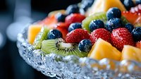 Fresh mixed fruit salad with strawberries, blueberries, kiwi and mango chunks arranged in crystal bowl, macro food photography with selective focus.