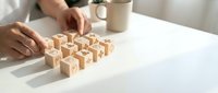 Hands arranging wooden cubes with engraved healthcare icons on a white table, symbolizing medical planning and health management concepts.
