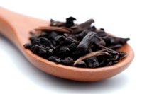 Dried black tea leaves in wooden spoon on white background, macro shot with selective focus. Natural organic loose leaf tea for brewing aromatic beverage.