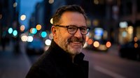 Smiling middle-aged Caucasian man with glasses and beard on city street at night with bokeh lights background for business and lifestyle concepts.