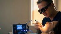 Professional male technician wearing protective eyewear operating precision laser equipment in modern laboratory setting for industrial manufacturing processes.