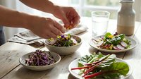 Hands preparing fresh healthy salad bowls with mixed greens, vegetables and colorful ingredients on wooden table for nutritious meal preparation.