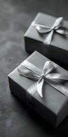 Elegant gift boxes wrapped in silver paper with shimmering ribbon bows on dark background, captured in monochrome style for luxury presentation.