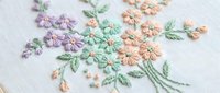 Delicate hand embroidered floral bouquet with purple and peach flowers on white fabric. Traditional needlework craft showcasing colorful thread artistry.