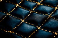 Luxury dark blue leather upholstery with golden stitching pattern creates elegant diamond quilted texture, close-up macro shot showing fine craftsmanship details.